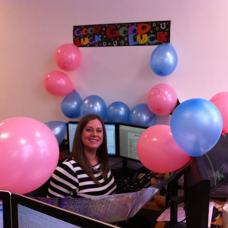 Shot of Jayne in Physio.co.uk office with pink and blue balloons and a banner on the wall saying good luck.