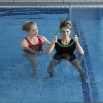 Wide shot of female in swimming pool holding a large ring in front of her with a physiotherapist holding on to females roght elbow.
