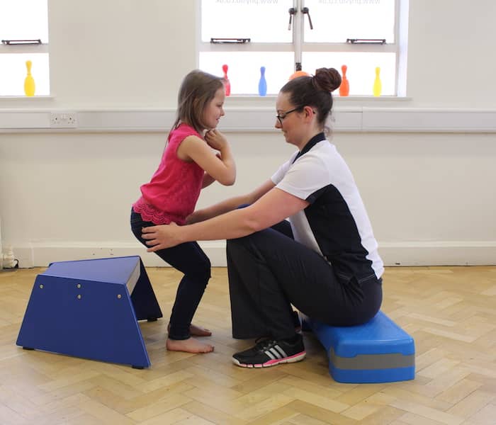 Side shot of little gitl squatting and therapist holding on to girls legs.