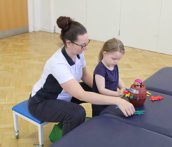 Wide shot of little girl playing a game with therapist next to her helping her play the game.